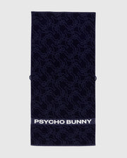 The Psycho Bunny TOWEL - B6A287F200 is a navy rectangular terrycloth cotton towel featuring an abstract bunny pattern and "PSYCHO BUNNY" in bold white letters along the bottom edge.