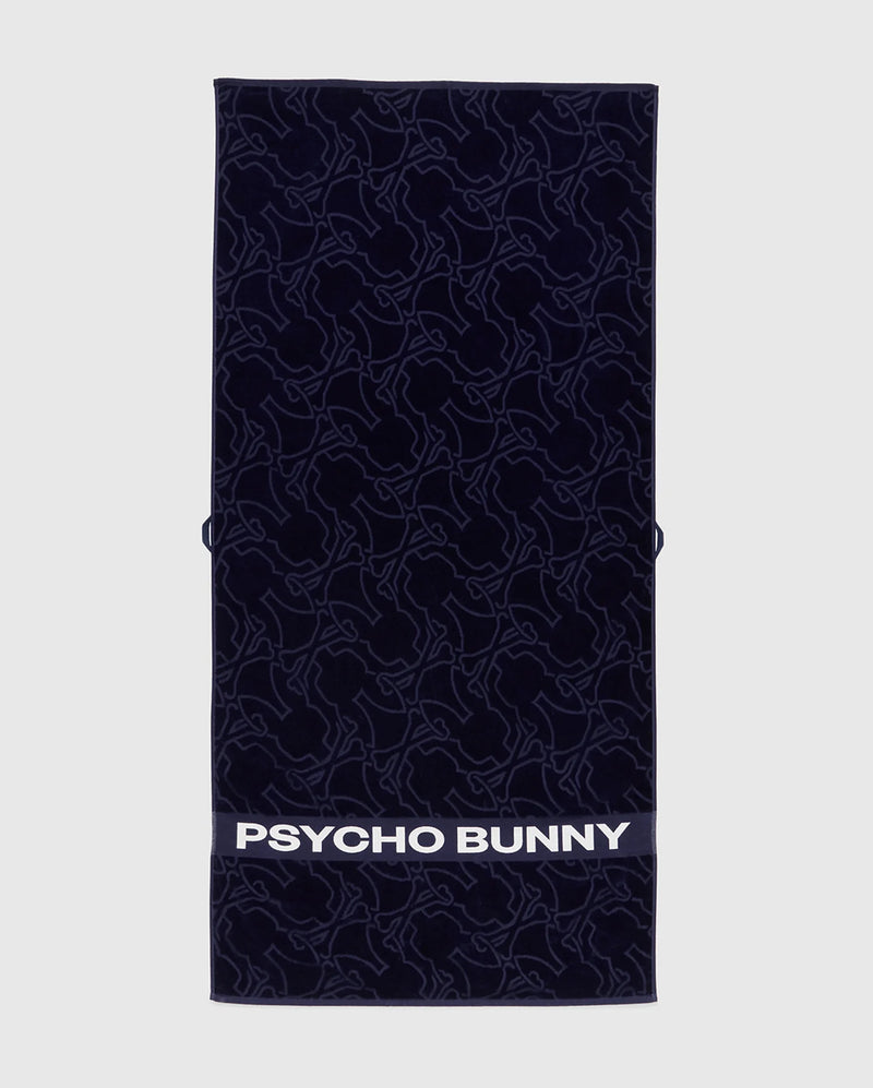 The Psycho Bunny TOWEL - B6A287F200 is a navy rectangular terrycloth cotton towel featuring an abstract bunny pattern and "PSYCHO BUNNY" in bold white letters along the bottom edge.