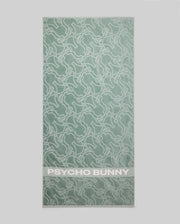 The Psycho Bunny TOWEL - B6A287F200 is a light green terrycloth cotton towel with a white abstract bunny pattern and "PSYCHO BUNNY" in bold white letters at the bottom.