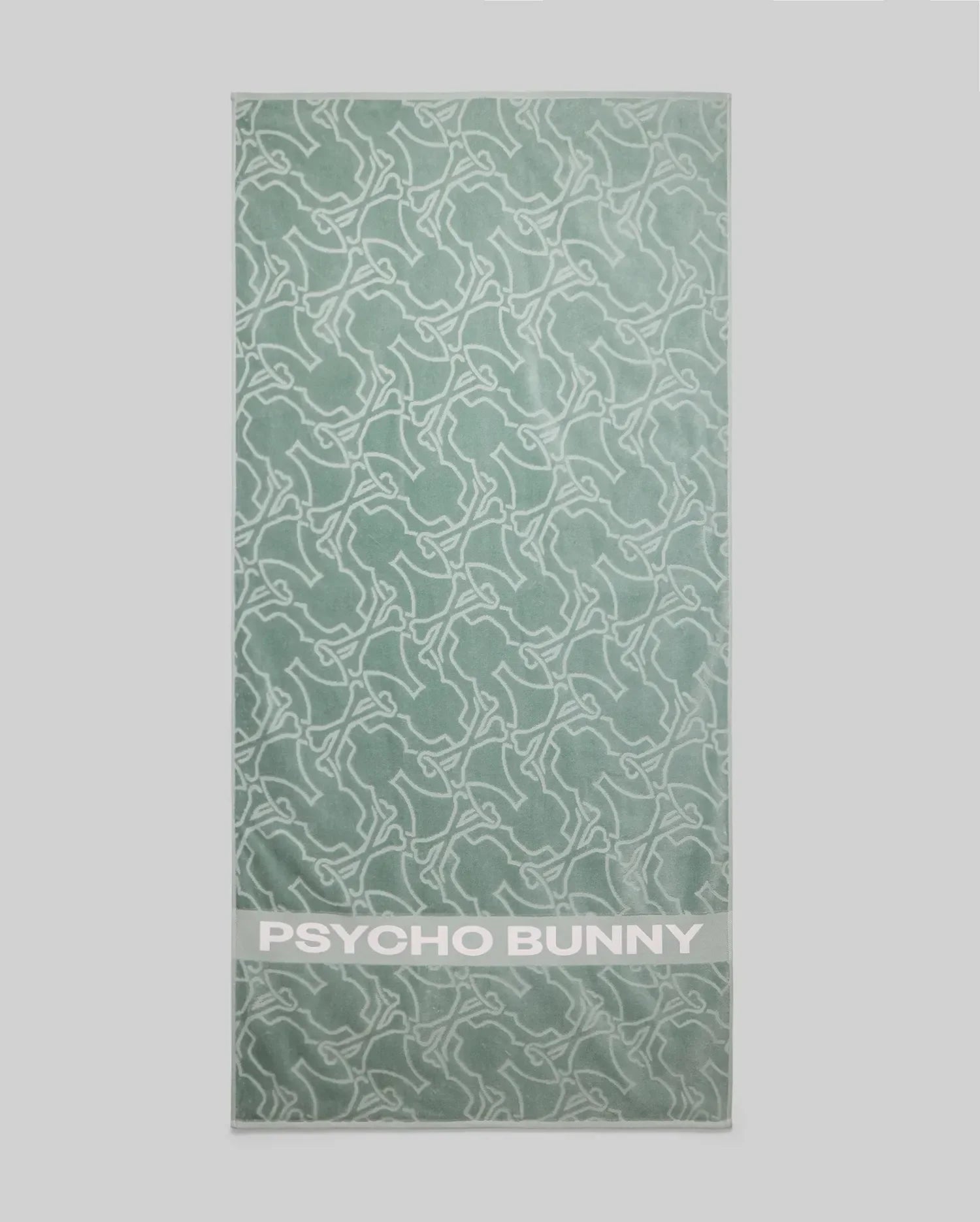The Psycho Bunny TOWEL - B6A287F200 is a light green terrycloth cotton towel with a white abstract bunny pattern and "PSYCHO BUNNY" in bold white letters at the bottom.