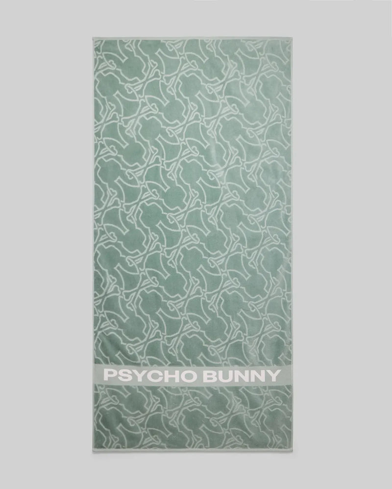 The Psycho Bunny TOWEL - B6A287F200 is a light green terrycloth cotton towel with a white abstract bunny pattern and "PSYCHO BUNNY" in bold white letters at the bottom.