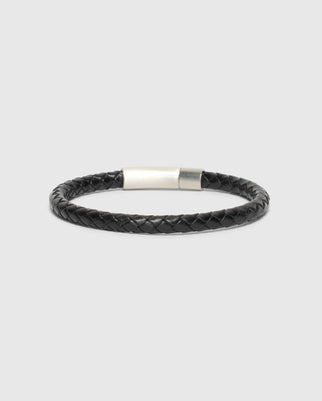 The Psycho Bunny MEN'S BRAIDED LEATHER BRACELET - B6A371E200 features durable black leather with a silver clasp, showcased on a plain gray background, making it a stylish accessory for men.