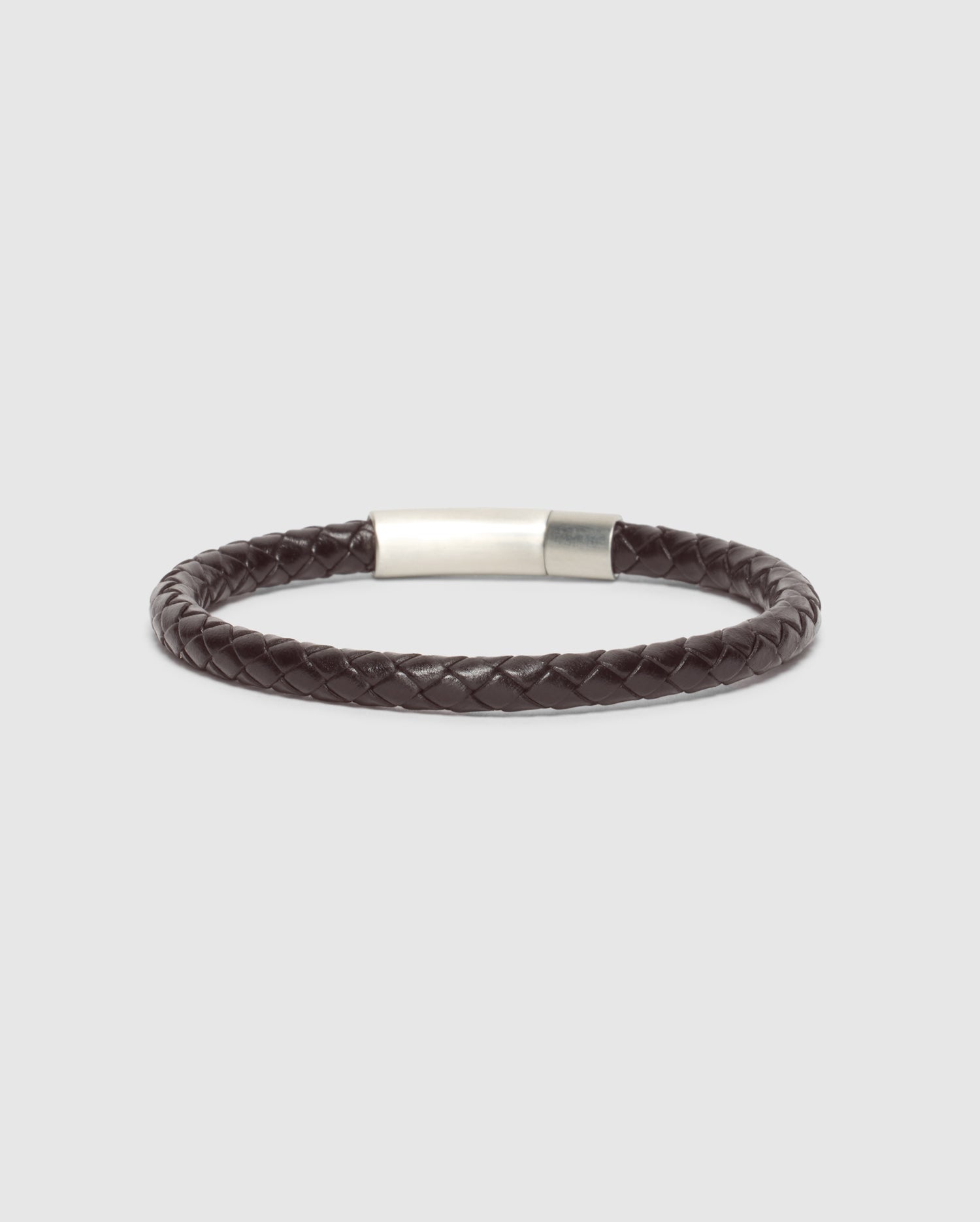The MEN'S BRAIDED LEATHER BRACELET - B6A371E200 by Psycho Bunny features an elegant dark brown design with a silver clasp, beautifully showcased on a light gray background.