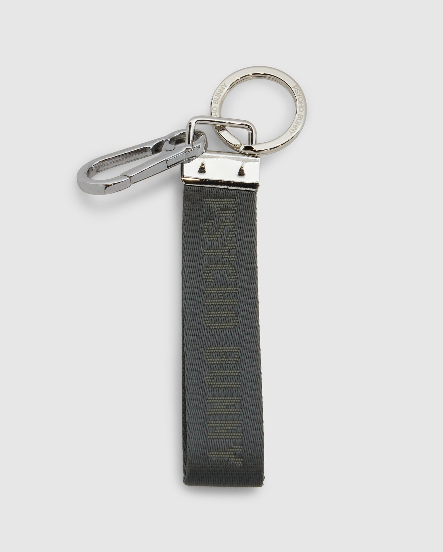 The Psycho Bunny WOVEN TAB KEYCHAIN - B6A374E200 features a silver carabiner and circular keyring. It includes a dark green, durable nylon strap with subtle matching text.