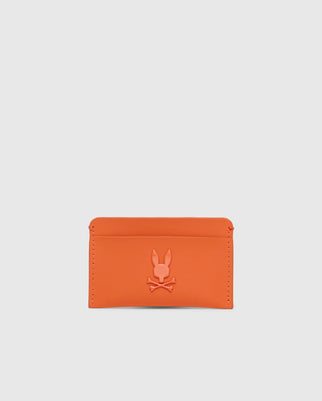 The Psycho Bunny MENS RUBBERIZED CARD CASE - B6A473F200 is a striking orange wallet featuring a debossed rabbit silhouette with crossed bones. Its minimalist design with clean stitching ensures your essentials are secure, all set against a plain white backdrop.