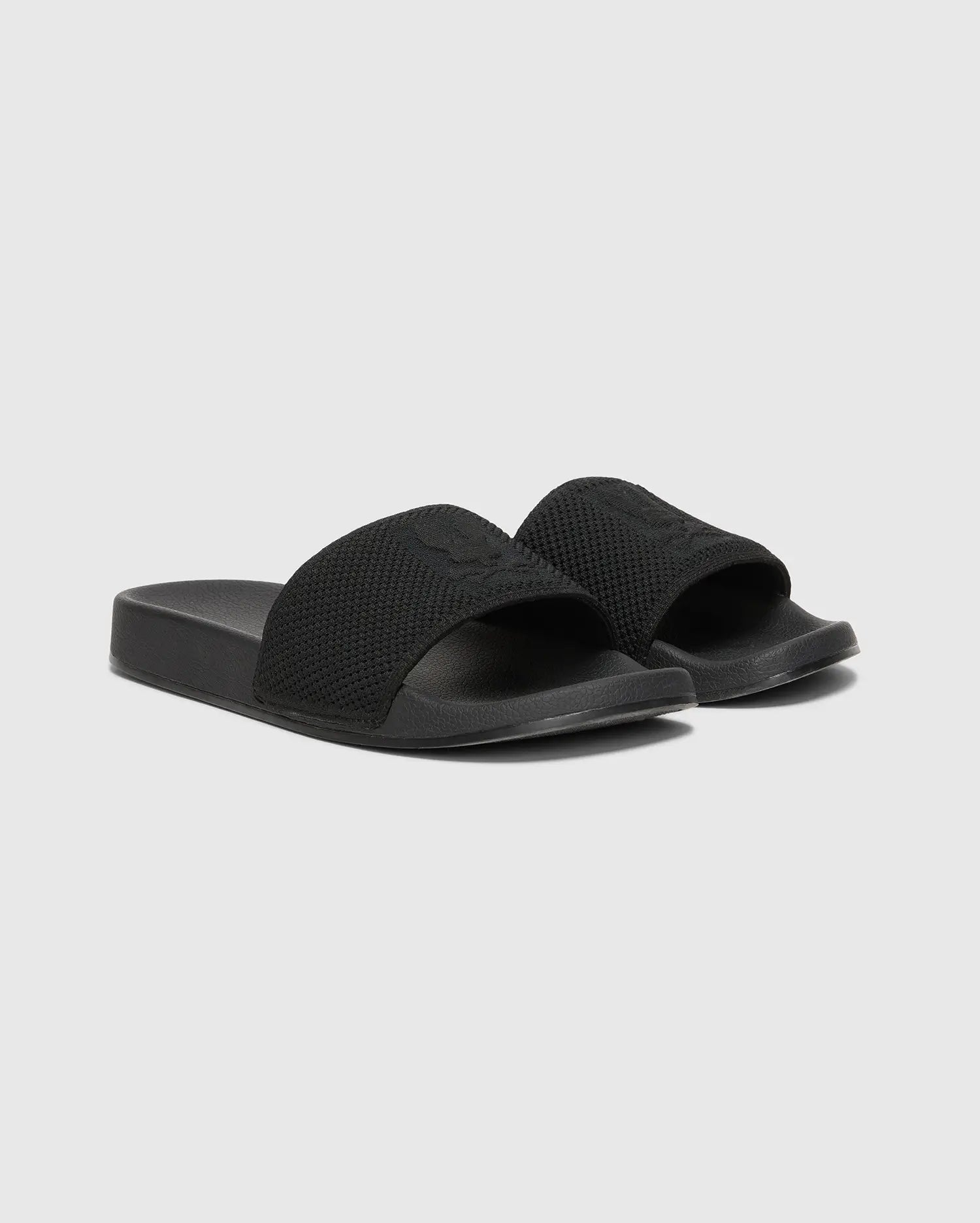 The MENS KNIT SLIDES - B6A474F200 by Psycho Bunny are black slide sandals with textured knit textile straps on a plain gray background. They feature an open-toe design, a molded footbed for comfort, and a flat, thick sole.