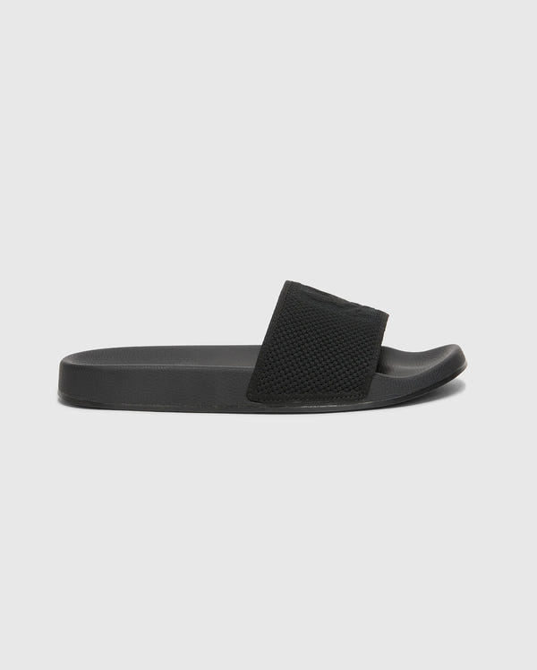 The Psycho Bunny MENS KNIT SLIDES - B6A474F200 are black slide sandals with textured straps, flat soles, and molded footbeds for comfort. Displayed against a white background, they feature an open toe design.