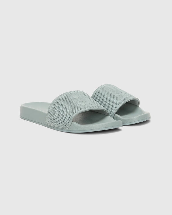 The Psycho Bunny MENS KNIT SLIDES - B6A474F200 are light green textured pool slides with open toes, a wide strap, and an ergonomically molded footbed, shown on a plain white background.