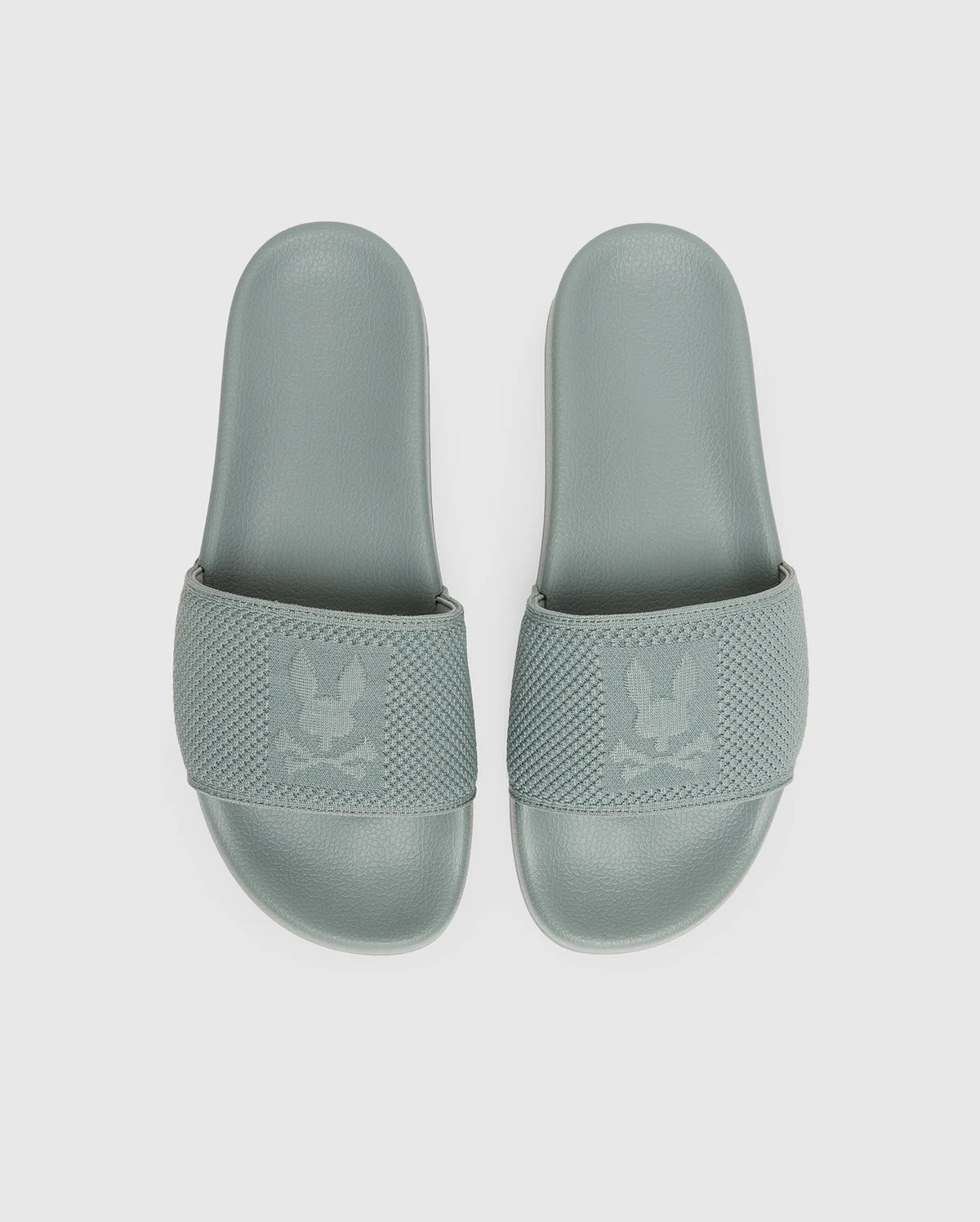 The Psycho Bunny MENS KNIT SLIDES - B6A474F200 feature sage green textured knit straps with a subtle eagle logo and an ergonomically molded footbed, shown against a plain white background.