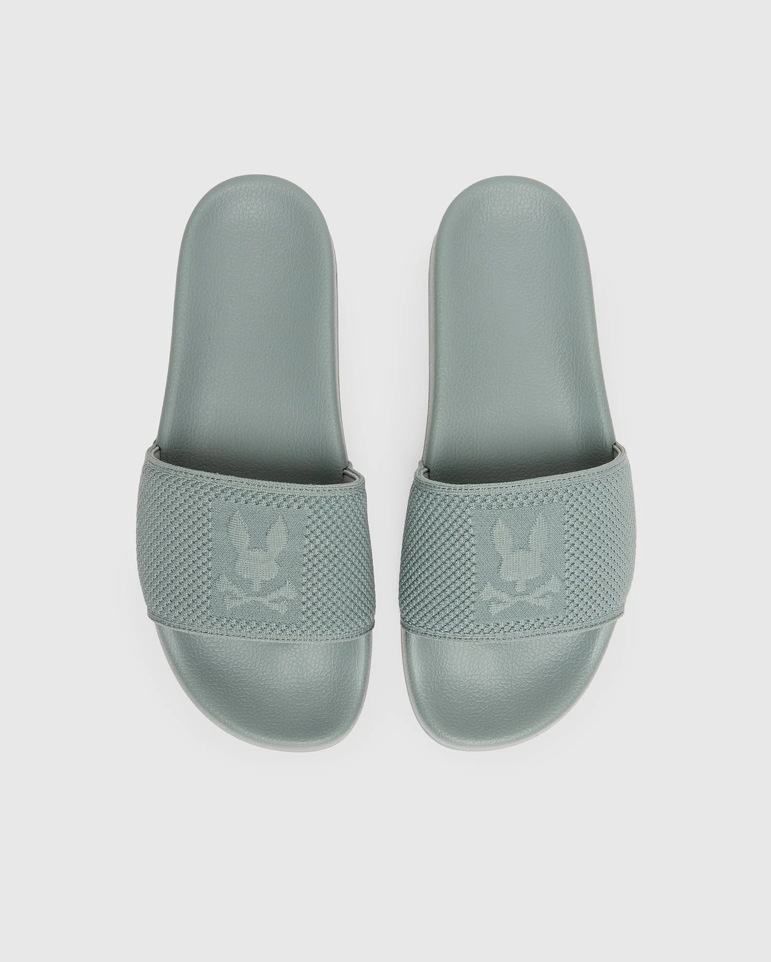 The Psycho Bunny MENS KNIT SLIDES - B6A474F200 feature sage green textured knit straps with a subtle eagle logo and an ergonomically molded footbed, shown against a plain white background.