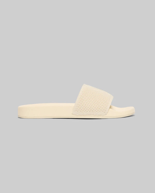 The Psycho Bunny MENS KNIT SLIDES - B6A474F200 features a single beige knit slide with a textured wide strap and molded footbed for summer comfort, shown against a plain light gray background.