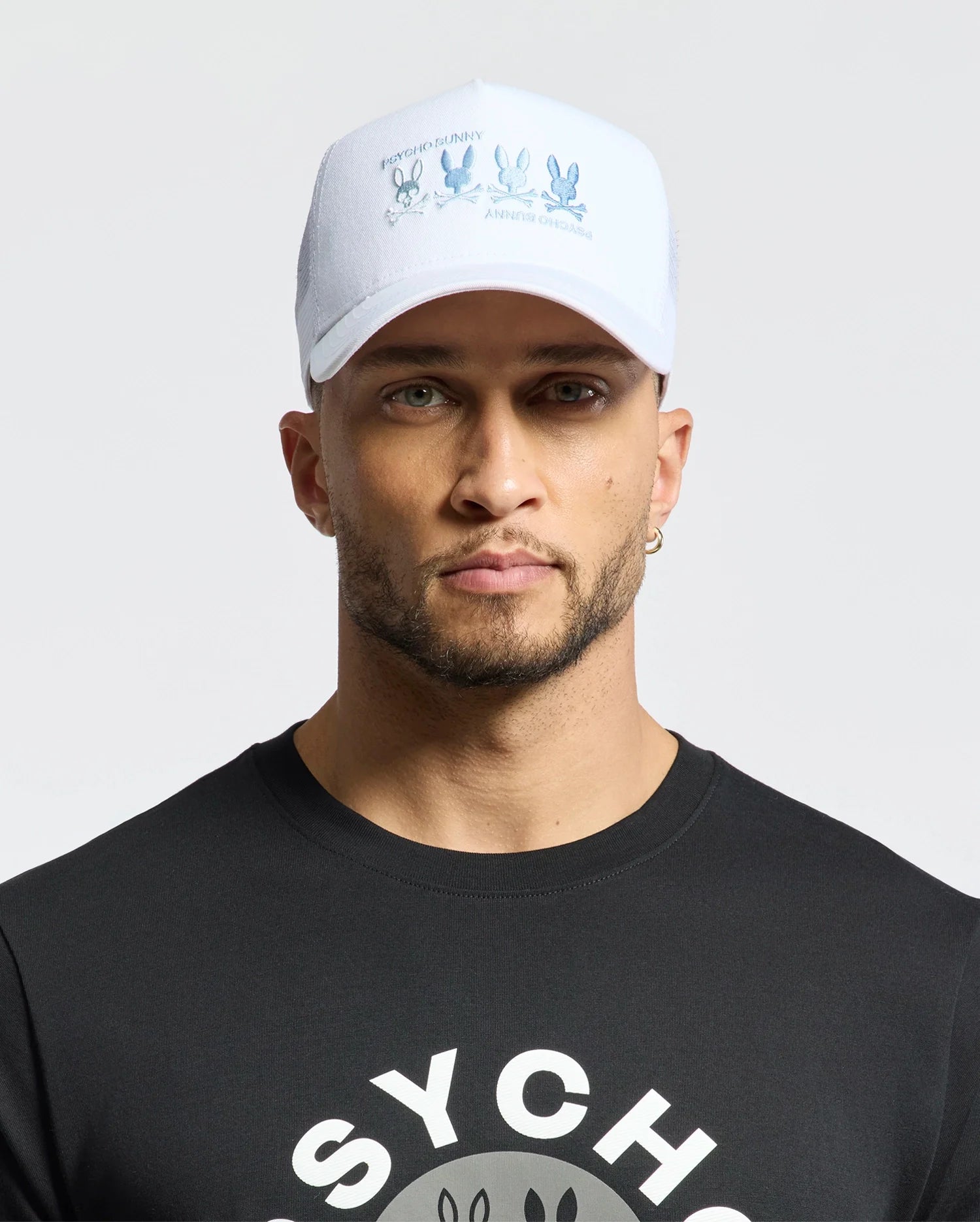 A person sports a Psycho Bunny Oceania Embroidered Graphic Trucker Hat and a black shirt with 