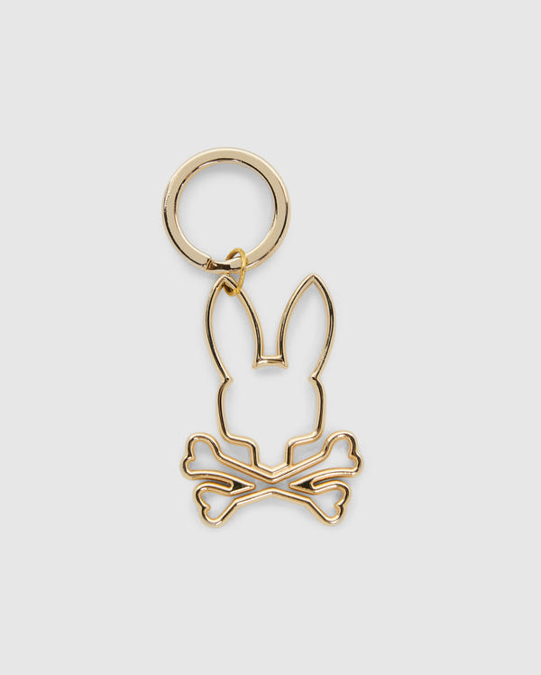The OUTLINE BUNNY KEYCHAIN - B6A565E200 by Psycho Bunny is a gold alloy piece with a minimalistic bunny outline featuring long ears over crossed bones, blending playful and edgy elements.