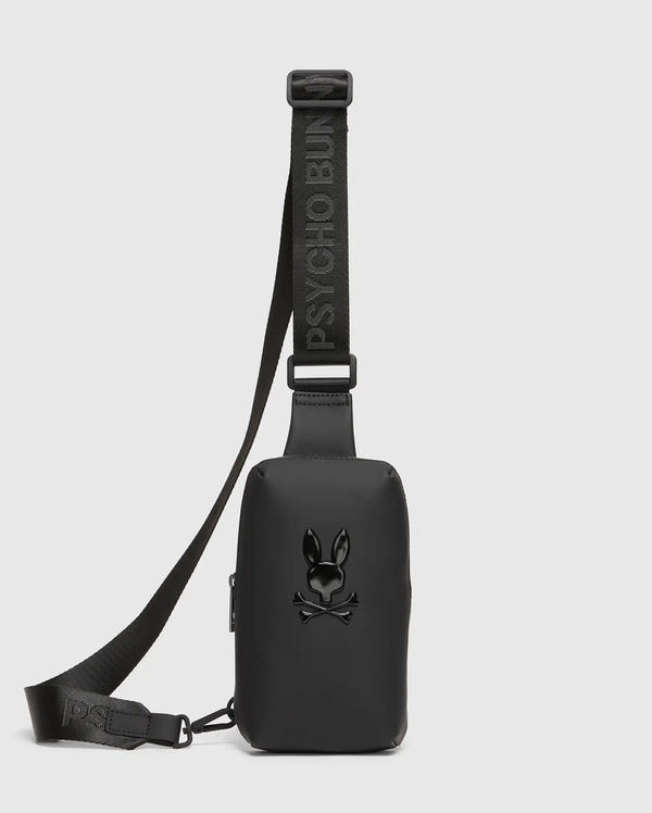 The MENS RUBBERIZED CROSSBODY - B6A635F200 from Psycho Bunny is a durable polyester black bag with "PSYCHO BUN" in raised letters on the strap. It displays a glossy skull and crossbones with bunny ears on the front, set against a plain white background.