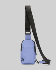The Psycho Bunny MENS RUBBERIZED CROSSBODY - B6A635F200 is a small, rectangular, light purple polyester bag with a black adjustable strap and zipper, shown against a plain gray background.