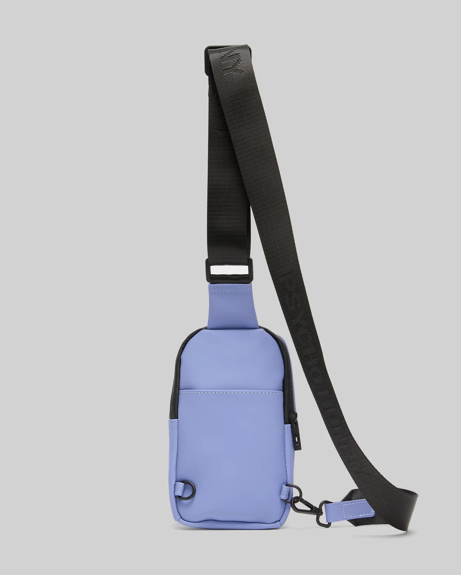 The Psycho Bunny MENS RUBBERIZED CROSSBODY - B6A635F200 is a small, rectangular, light purple polyester bag with a black adjustable strap and zipper, shown against a plain gray background.