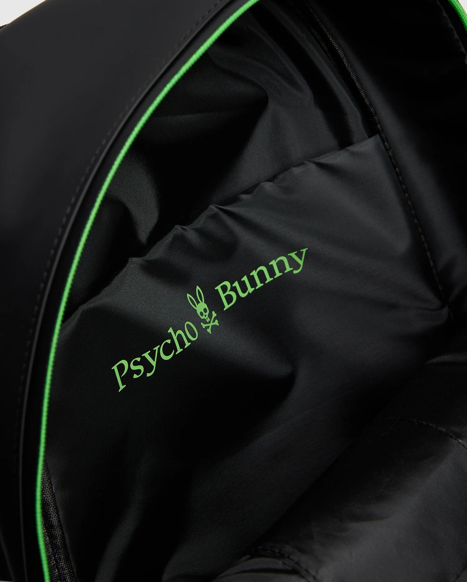 Close-up of a MENS RUBBERIZED BACKPACK - B6A637F200 interior featuring the green Psycho Bunny logo with a bunny skull design. The durable lining shows off its smooth fabric and subtle stitching, highlighting its functionality.