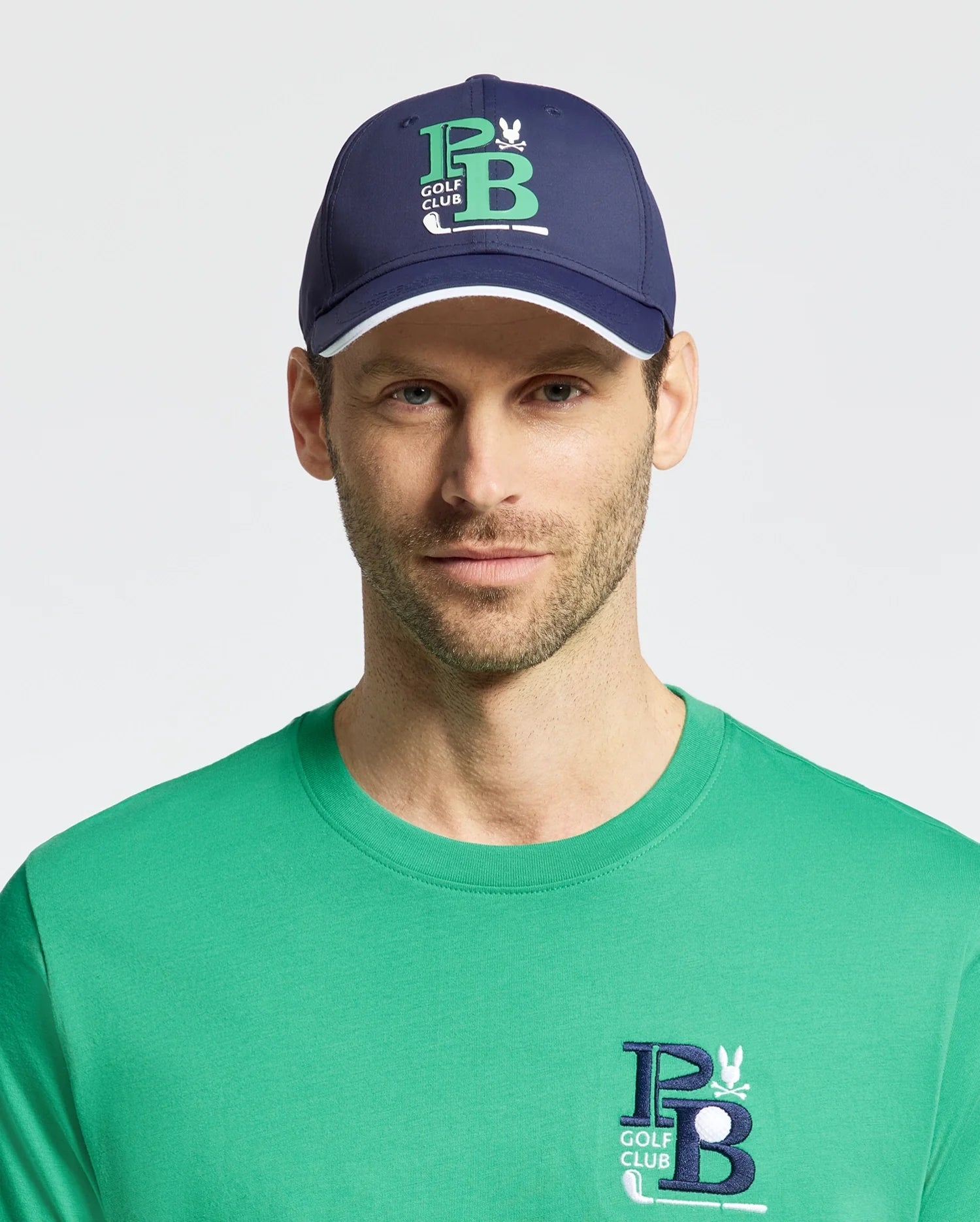 A man sports the MENS DENIS SPORT CAP by Psycho Bunny in navy, with 