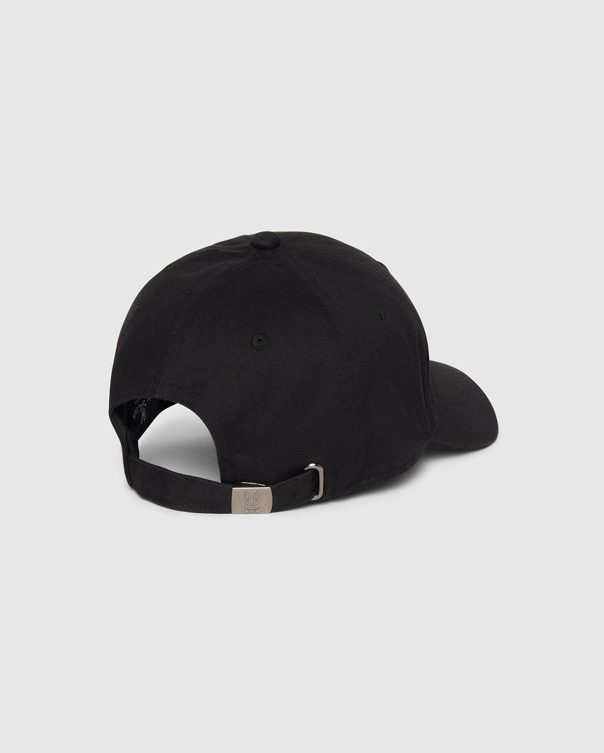 This image showcases the Psycho Bunny Men's Classic Baseball Cap (B6A816A1HT) in black, viewed from the rear. Made of 100% cotton, the cap features a curved brim, an adjustable strap with a metal buckle at the back, ventilation eyelets, and an embroidered Bunny logo. The background is plain white or light grey.
