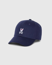 Product Description: The MENS CLASSIC BASEBALL CAP - B6A816A1HT by Psycho Bunny is a classic navy blue six-panel cotton twill cap, showcasing a pink-eared white bunny logo above a crossbones design embroidered on the front against a light gray background.