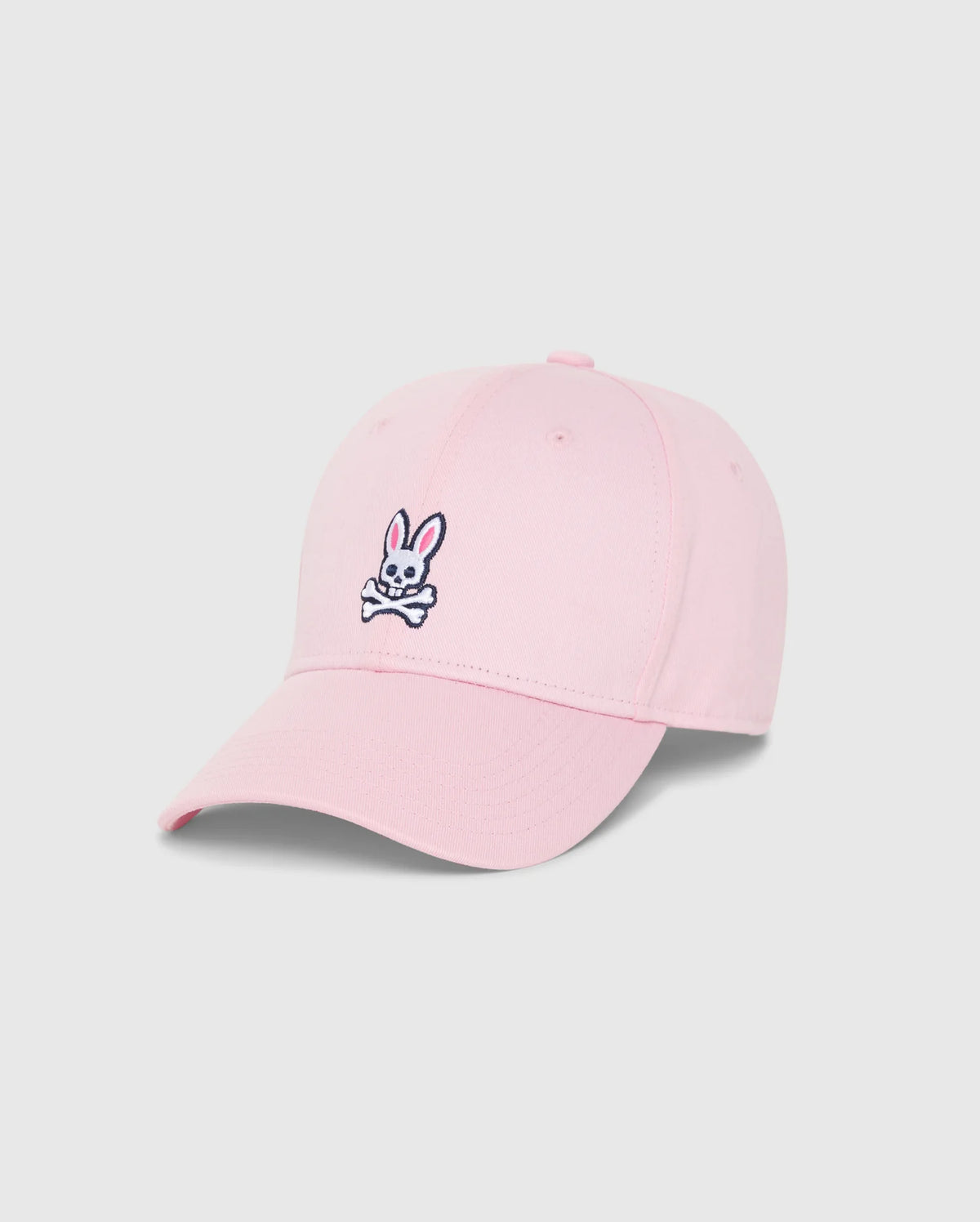 The MENS CLASSIC BASEBALL CAP - B6A816A1HT by Psycho Bunny is a timeless pink accessory made from six-panel cotton twill. It prominently features the brand's iconic black and white embroidered Bunny logo, showcasing a cartoon rabbit head and crossed bones. The cap is elegantly showcased on a plain white background.