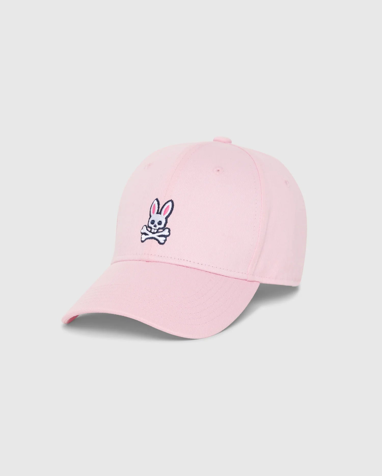 The MENS CLASSIC BASEBALL CAP - B6A816A1HT by Psycho Bunny is a timeless pink accessory made from six-panel cotton twill. It prominently features the brand's iconic black and white embroidered Bunny logo, showcasing a cartoon rabbit head and crossed bones. The cap is elegantly showcased on a plain white background.
