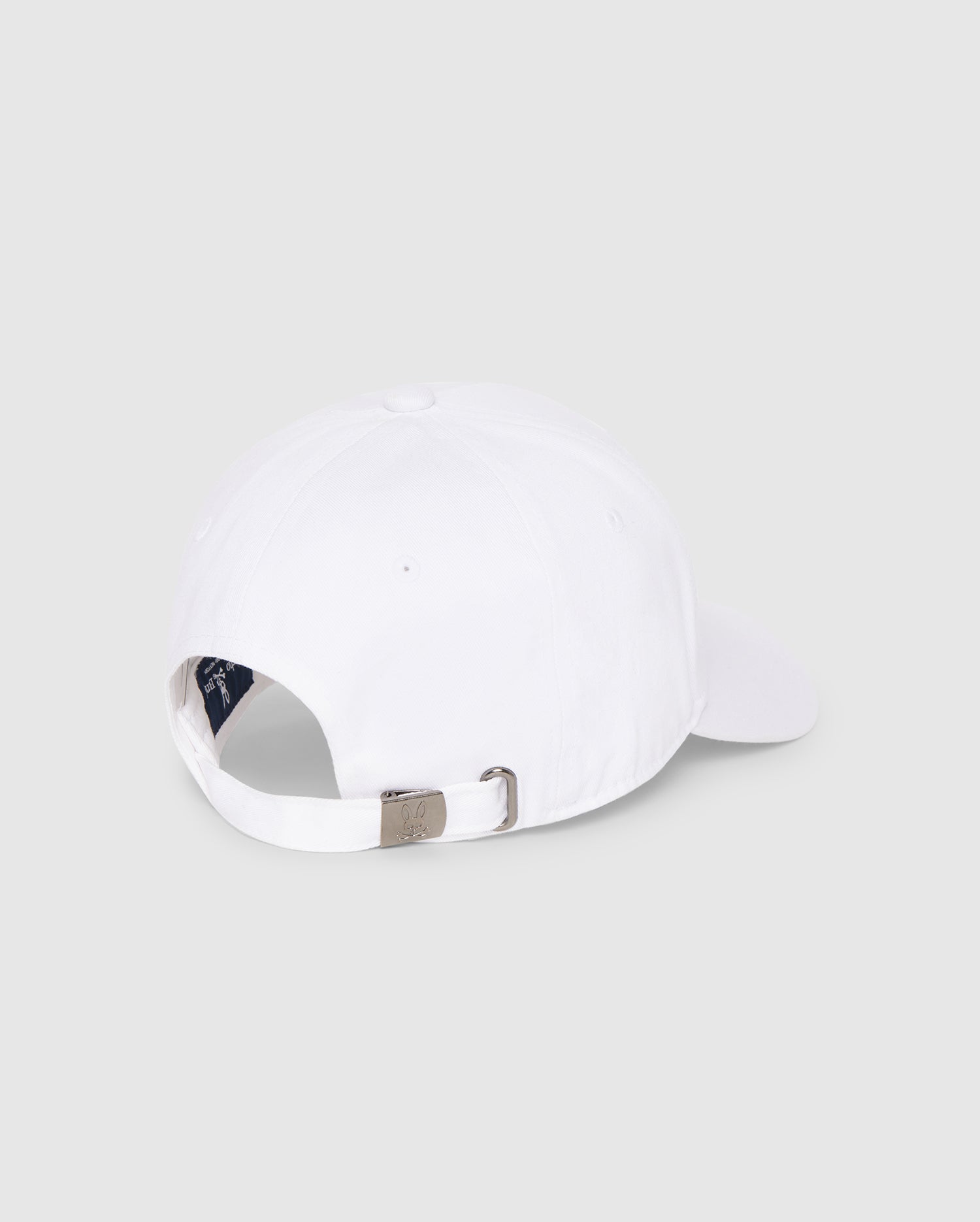 This is a rear view of the MENS CLASSIC BASEBALL CAP - B6A816A1HT from Psycho Bunny, showcasing an adjustable strap with a metallic buckle for a customized fit and a small opening above the strap. The interior of the cap is partially visible against a plain, light gray background.