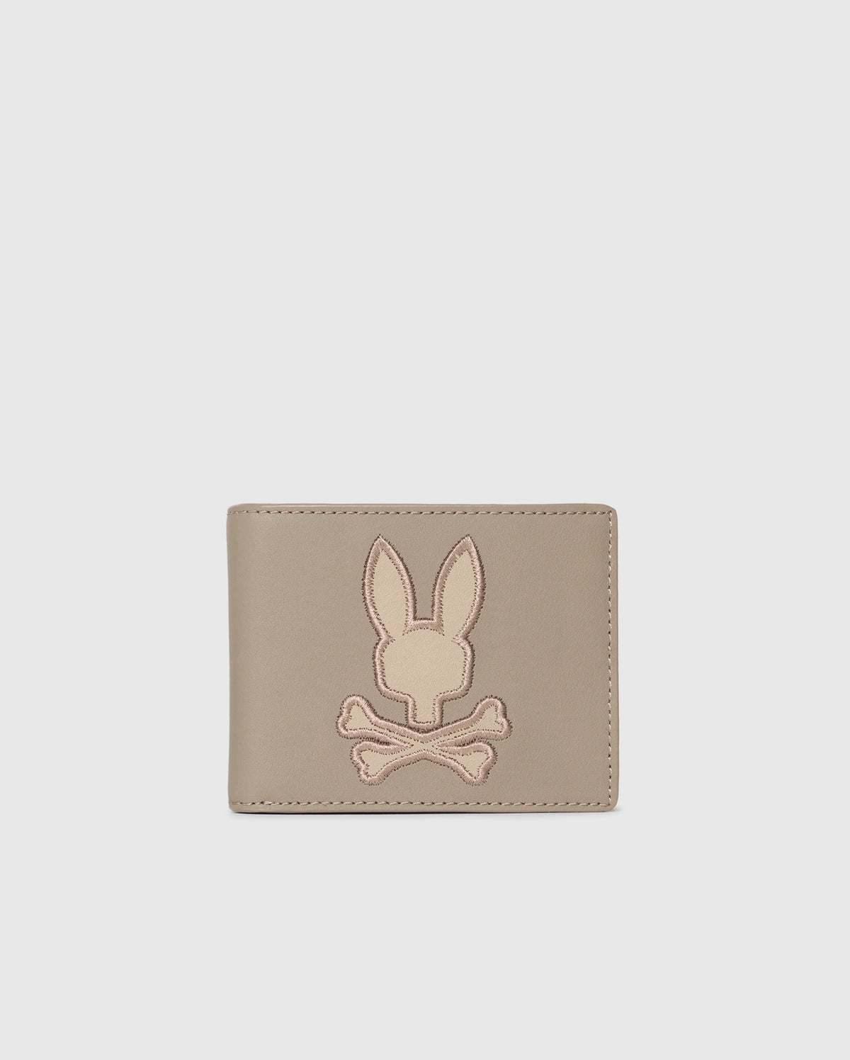 The MENS LEATHER WALLET - B6A868D200 by Psycho Bunny features a stitched bunny head over crossed bones on its light gray front. Its premium leather and unique design make it a luxurious accessory for the discerning.