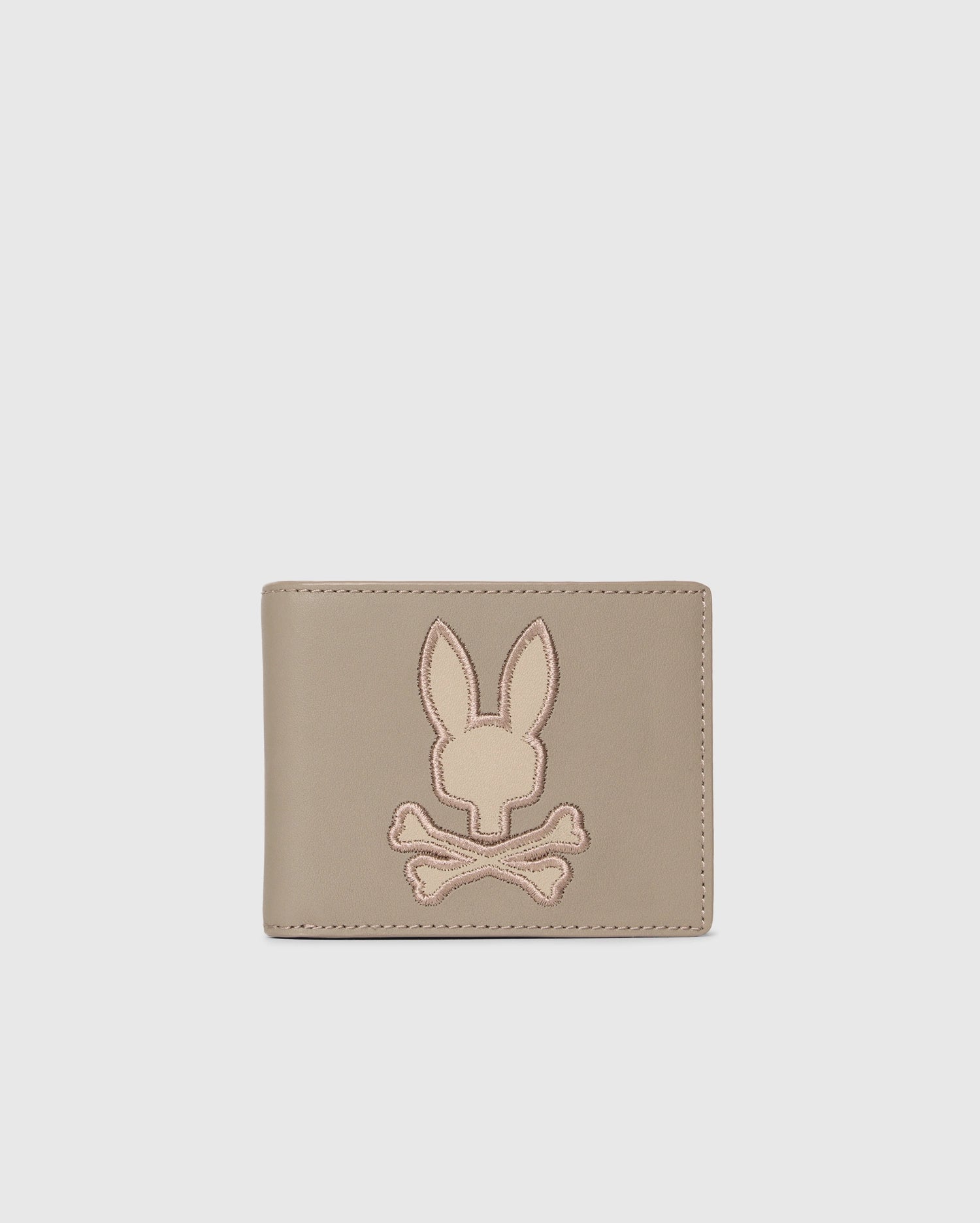 The MENS LEATHER WALLET - B6A868D200 by Psycho Bunny features a stitched bunny head over crossed bones on its light gray front. Its premium leather and unique design make it a luxurious accessory for the discerning.