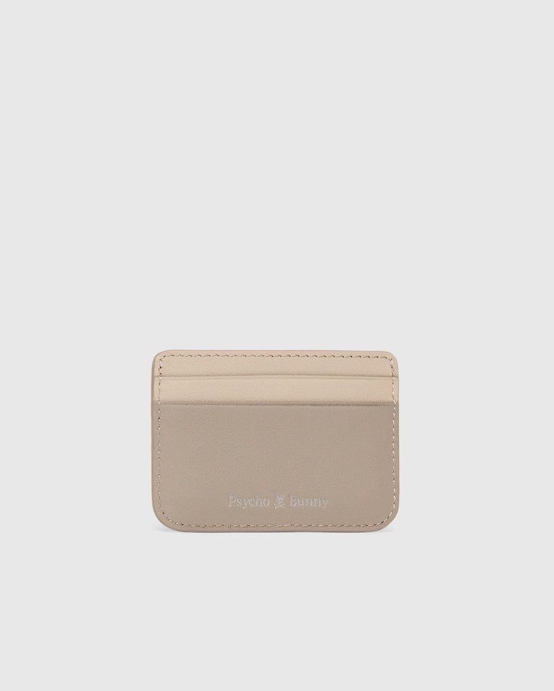 The MENS LEATHER CARD CASE - B6A869D200 by Psycho Bunny is a premium beige leather cardholder with three front slots and a silver "Psycho Bunny" embossing near the bottom center, minimal edge stitching on a plain light gray background.