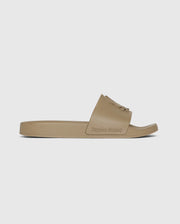 A beige MENS LOGO SLIDES - B6A910U1FT featuring a wide single strap with an embossed rabbit skull logo and the brand name "Psycho Bunny" on the side of the molded footbed. The slide boasts a flat sole, an open toe design, and a treaded rubber outsole for extra grip.