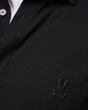 Close-up of the Psycho Bunny MENS ARTHUR JERSEY SHIRT - B6C748D200 in rich black, showcasing a small embroidered logo on the chest. Made from stretch Pima cotton jersey fabric, the playful design features a rabbit's head with crossed bones, adding a unique twist to this classic look.