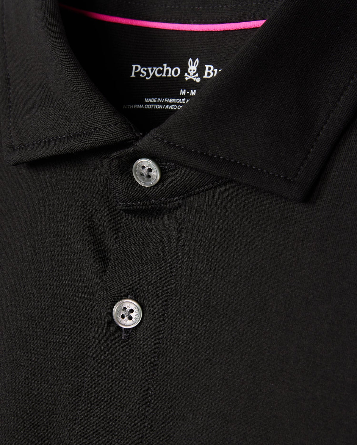 Close-up of a black MENS ARTHUR JERSEY SHIRT - B6C748D200 collar and upper chest area, featuring two buttons slightly undone. The brand "Psycho Bunny" is visible on the inside of the collar, along with the size "M." The stitching and jersey fabric texture in stretch Pima cotton are clearly depicted.