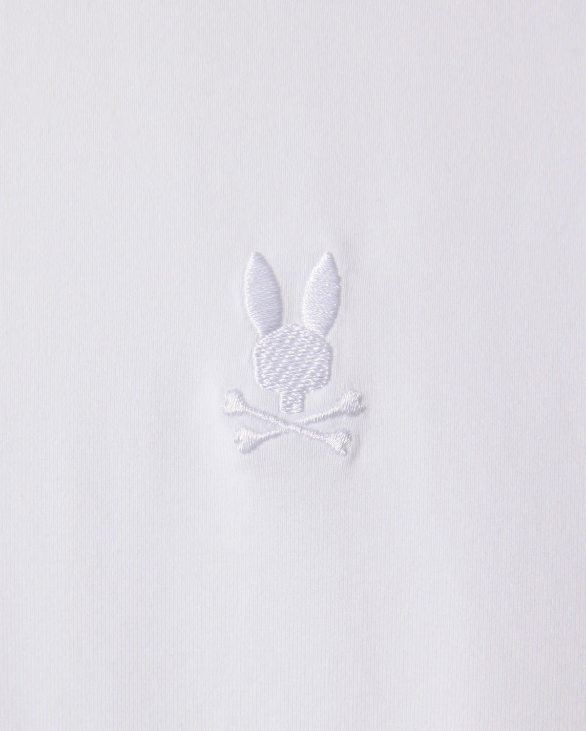 White embroidery on stretch Pima cotton fabric depicts a stylized rabbit head with long ears above a pair of crossed bones. The design, featured on the Psycho Bunny Men's Arthur Jersey Shirt (B6C748D200), is simple and monochromatic.