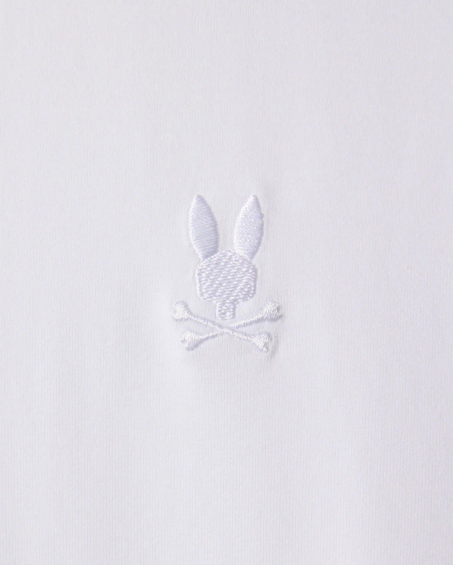 White embroidery on stretch Pima cotton fabric depicts a stylized rabbit head with long ears above a pair of crossed bones. The design, featured on the Psycho Bunny Men's Arthur Jersey Shirt (B6C748D200), is simple and monochromatic.
