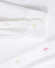 Close-up of a Psycho Bunny's Mens Arthur Jersey Shirt (B6C748D200) showcasing its buttoned cuff and two front buttons. Crafted from crisp, clean stretch Pima cotton, the fabric offers a subtle pop with one buttonhole stitched in pink thread, enhancing the elegance of this all-white shirt.