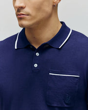 A man, shown from the lower face to upper torso, wears the Psycho Bunny MENS LONGFORD FINE KNIT POLO - B6E500F200 in navy with white trim on the collar and pocket, made from fine-knit jersey, as he faces slightly left.