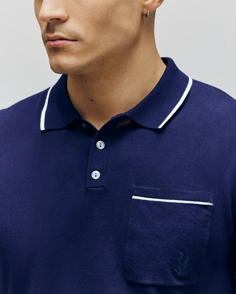 A man, shown from the lower face to upper torso, wears the Psycho Bunny MENS LONGFORD FINE KNIT POLO - B6E500F200 in navy with white trim on the collar and pocket, made from fine-knit jersey, as he faces slightly left.