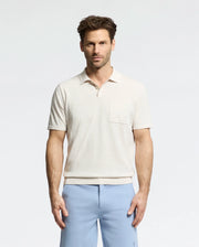 A man stands against a plain background wearing the Psycho Bunny MENS LONGFORD FINE KNIT POLO (B6E500F200) with light blue pants. With short, styled hair, he maintains a neutral expression while facing the camera.