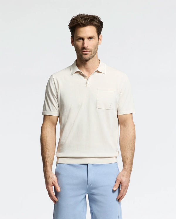 A man stands against a plain background wearing the Psycho Bunny MENS LONGFORD FINE KNIT POLO (B6E500F200) with light blue pants. With short, styled hair, he maintains a neutral expression while facing the camera.