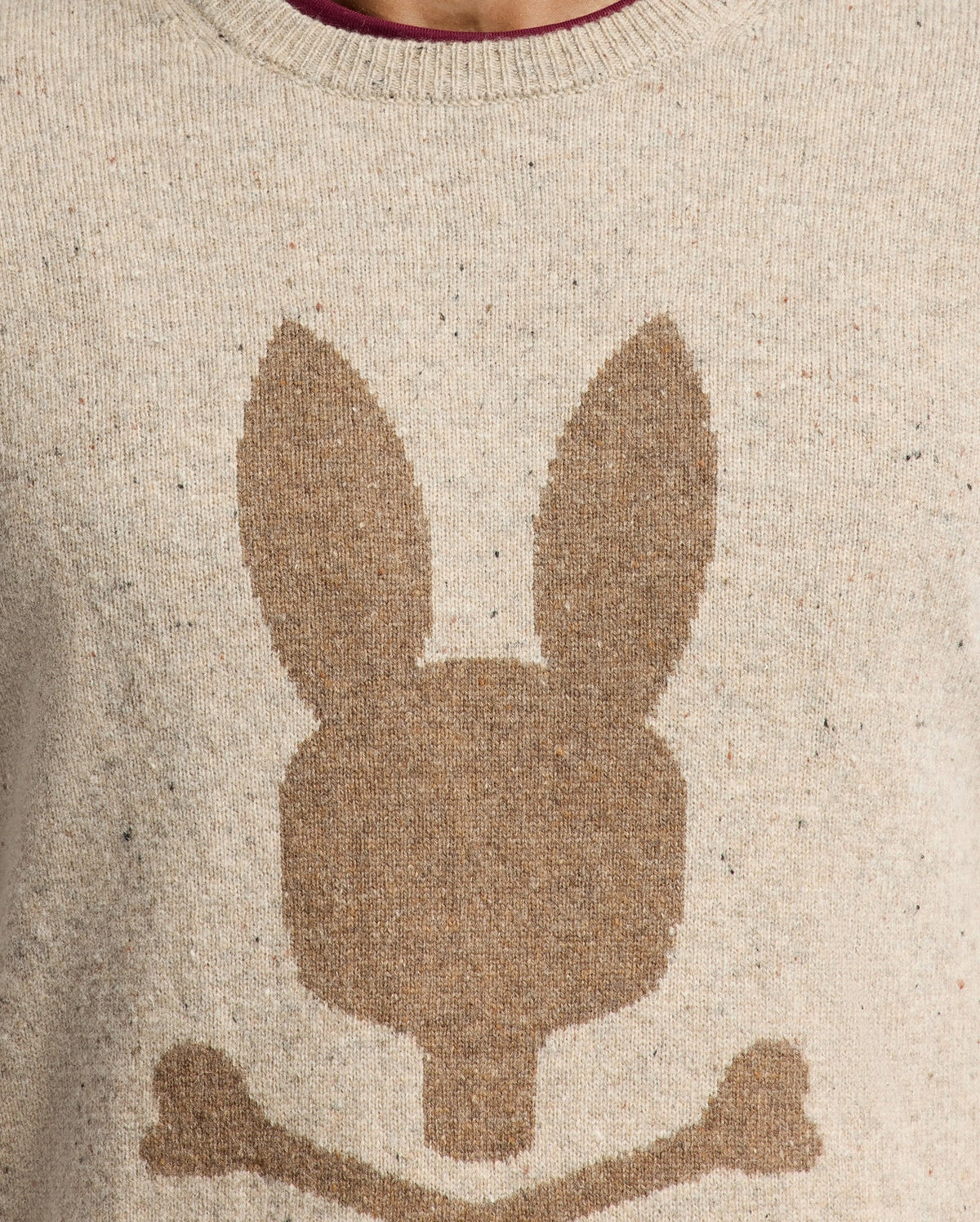 The Psycho Bunny MENS LINCOLN MERINO WOOL SWEATER - B6E831E200 features a beige color with a bold, oversized brown bunny head and crossed bones design, reminiscent of a skull and crossbones motif, making it perfect for cold weather.