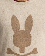 The Psycho Bunny MENS LINCOLN MERINO WOOL SWEATER - B6E831E200 features a beige color with a bold, oversized brown bunny head and crossed bones design, reminiscent of a skull and crossbones motif, making it perfect for cold weather.