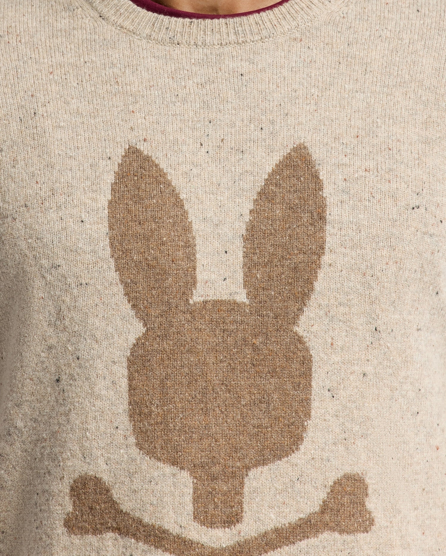The Psycho Bunny MENS LINCOLN MERINO WOOL SWEATER - B6E831E200 features a beige color with a bold, oversized brown bunny head and crossed bones design, reminiscent of a skull and crossbones motif, making it perfect for cold weather.