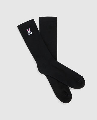 These black fashion socks from Psycho Bunny, titled **MENS FASHION SOCKS - B6F486C200**, showcase a subtle embroidered detail of a pink-eared, white bunny skull and crossbones on the side. Expertly crafted from luxurious Pima cotton, they originate from Peru and are elegantly displayed against a plain white background.
