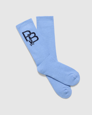 A pair of light blue Psycho Bunny MENS PB SPORT SOCK - B6F501F200, featuring a black "PB" logo and small leaf design, are displayed in a crossed position on a plain white background, offering competitive comfort.