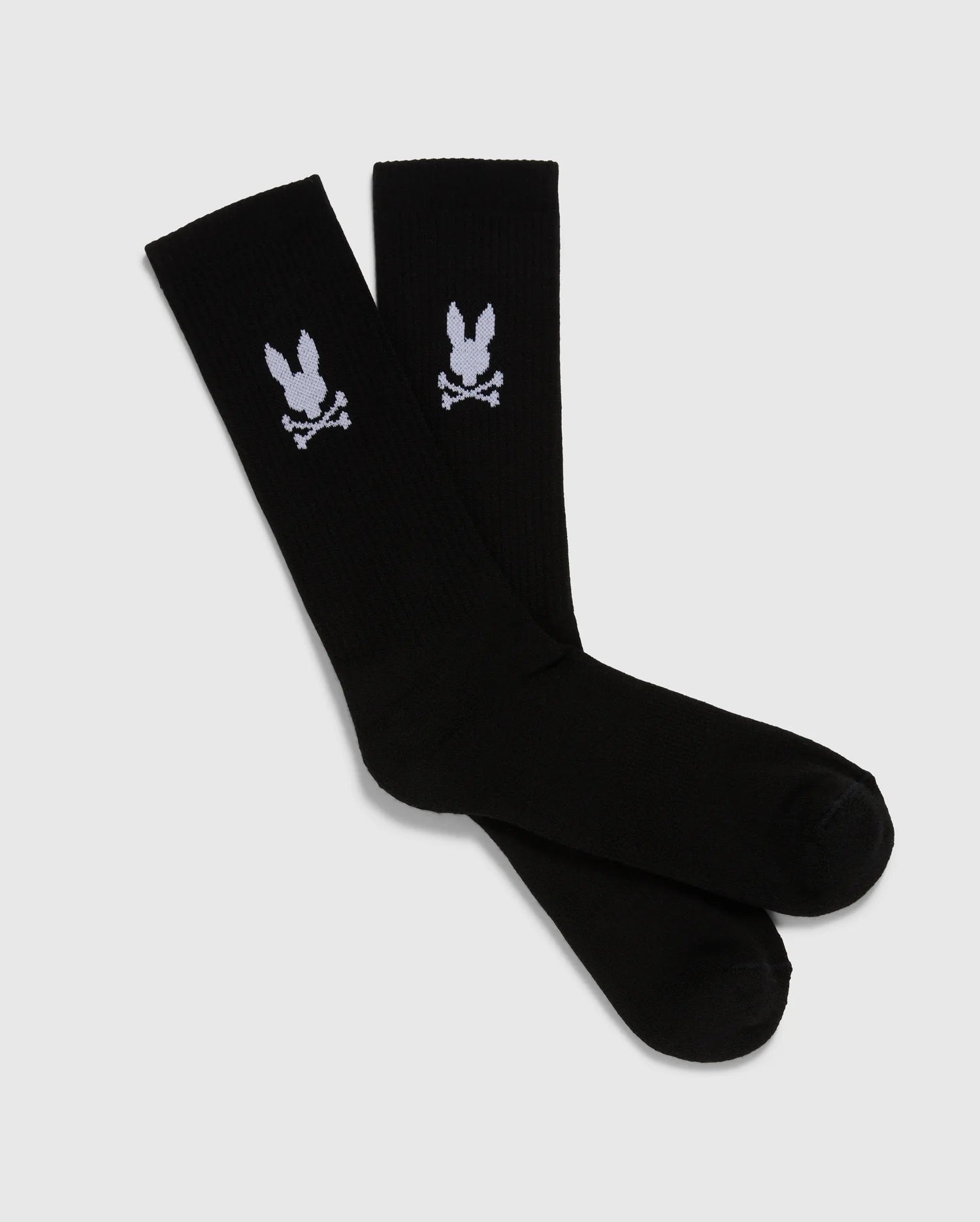 A pack of 3 pairs of black men's knee-high sport socks from the Psycho Bunny brand, featuring a white skull and crossbones symbol with bunny ears on each sock. Made from luxurious Peruvian pima cotton, these MENS 3 PACK SPORT SOCK - B6F997D200 socks are displayed positioned overlapping each other against a plain, light gray background.