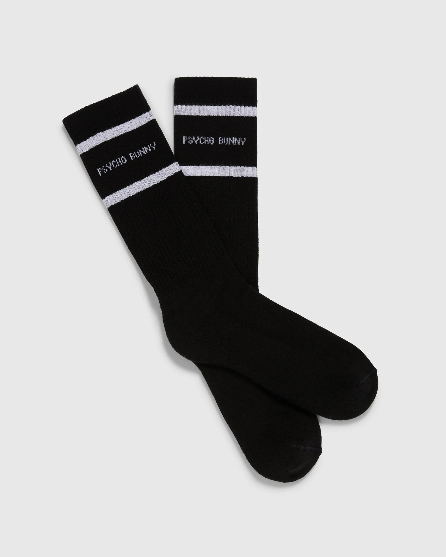 Introducing the MENS 3 PACK SPORT SOCK - B6F997D200 by Psycho Bunny: This pack includes 3 pairs of black crew sport socks, each adorned with white stripes near the top. Crafted from luxurious Peruvian pima cotton, these socks feature the "Psycho Bunny" text in white just below the stripes, all set against a plain light gray backdrop.
