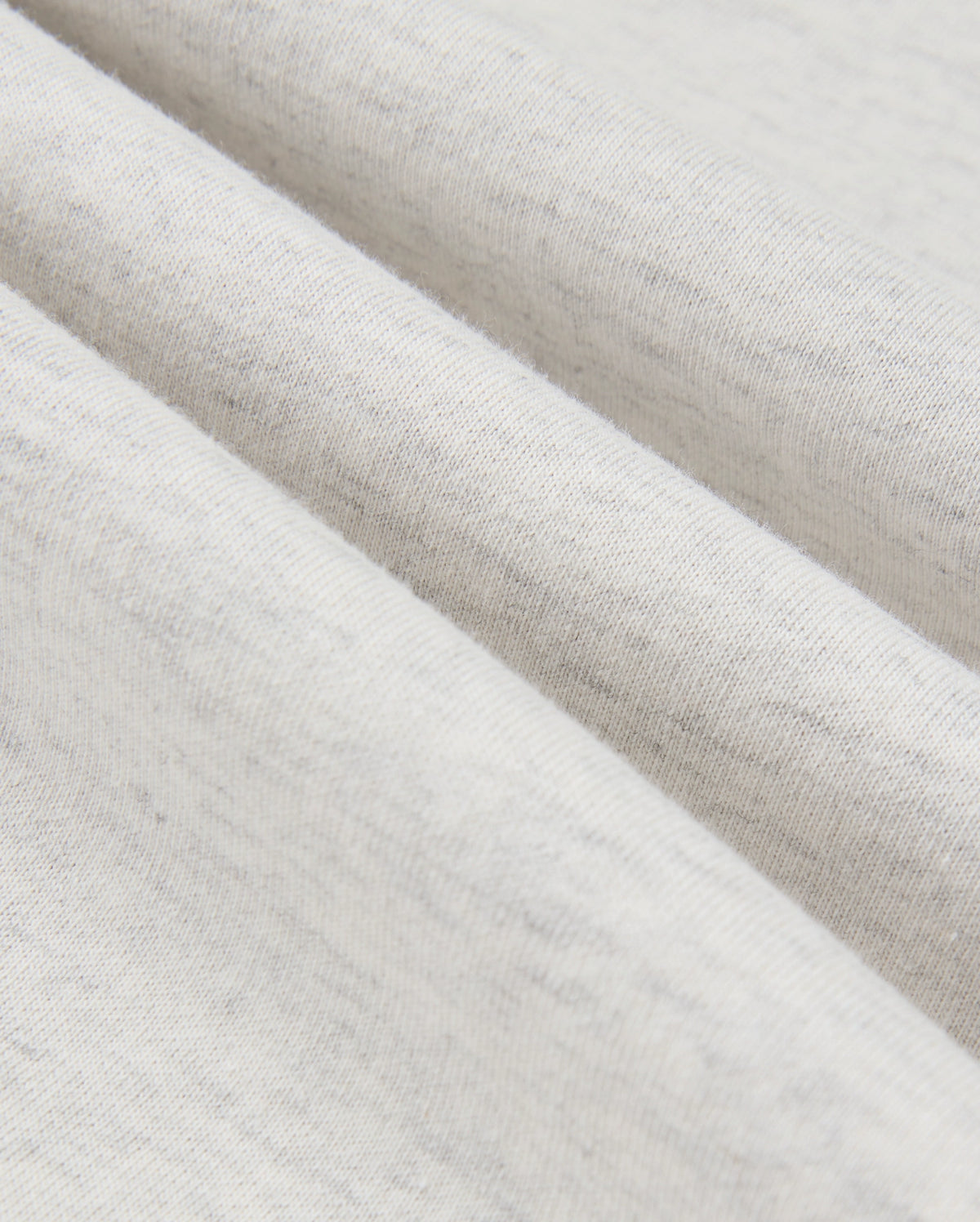 Close-up of a gently folded, light gray fabric from the MENS JAMES PREMIUM HOODIE - B6H789D200 by Psycho Bunny, showcasing its soft texture and subtle specks. The folds create slight shadows that accentuate the material's smoothness and fine weave.