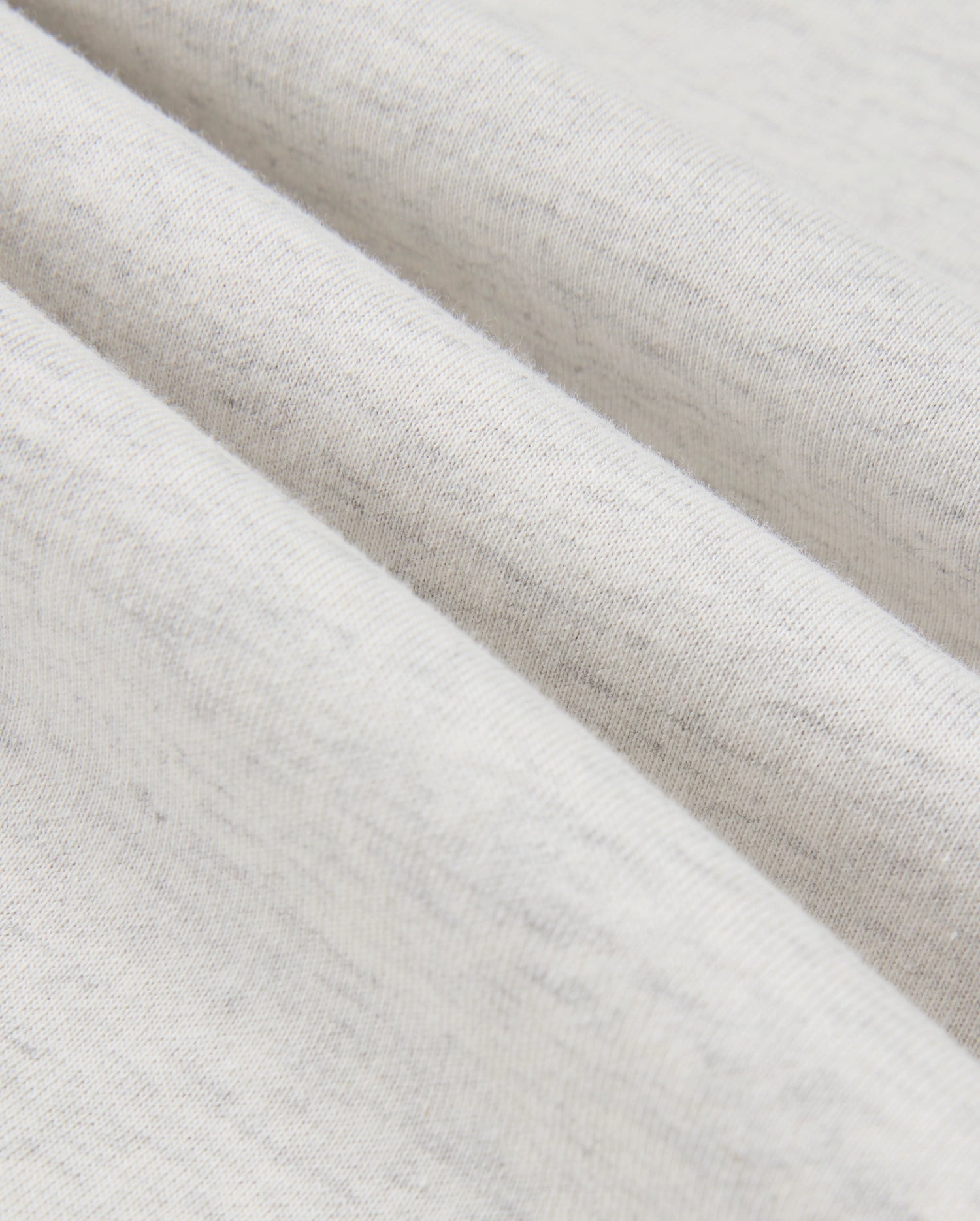 Close-up of a gently folded, light gray fabric from the MENS JAMES PREMIUM HOODIE - B6H789D200 by Psycho Bunny, showcasing its soft texture and subtle specks. The folds create slight shadows that accentuate the material's smoothness and fine weave.