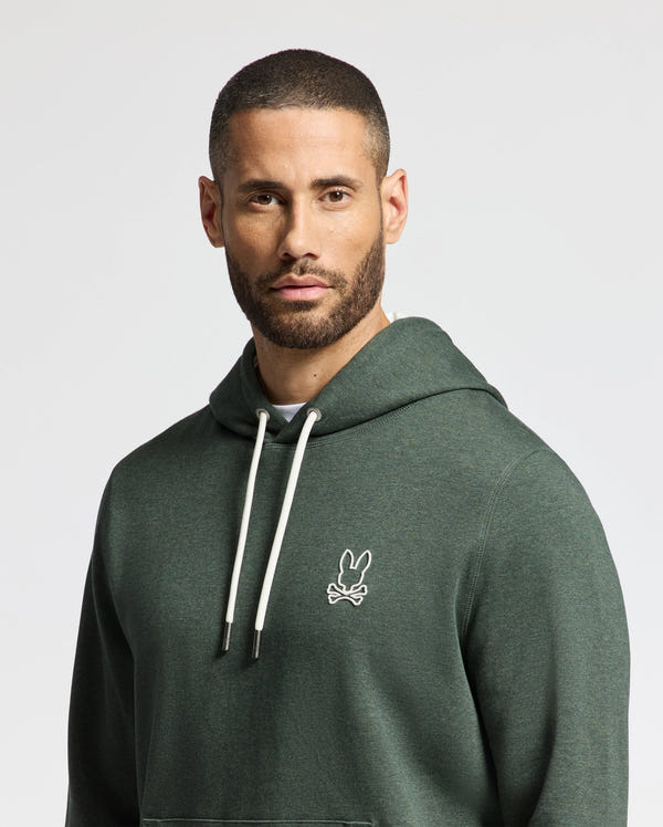 A person wearing the stylish Psycho Bunny MENS JAMES PREMIUM HOODIE - B6H789D200, adorned with the iconic bunny logo, stands against a plain background. This lightweight green hoodie with white drawstrings perfectly complements his beard and short hair.